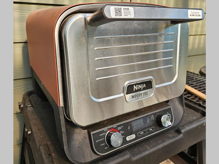 Small pizza oven sitting on a black shelf outdoors beside a house