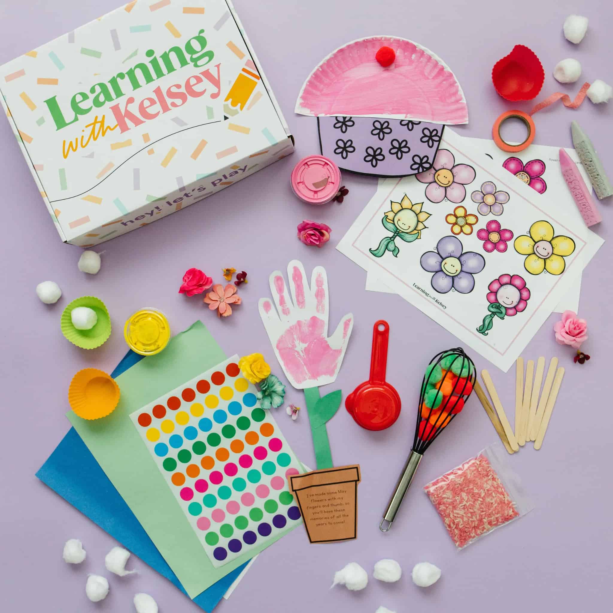 A flat lay of colorful craft materials, activity sheets with flowers, a painted cupcake cutout, stickers, colored paper, and a Learning with Kelsey box on a pastel purple background—perfect for preventing summer learning loss.