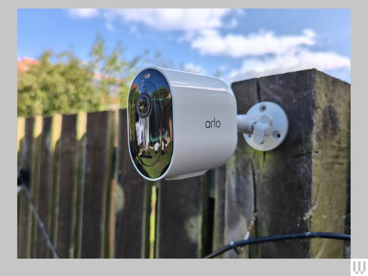 White oval-shaped outdoor security camera attached to wooden fence